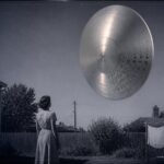 A woman in her Oklahoma City yard watches a silent, 80-foot metallic disc with twelve occupant silhouettes visible in its windows, late August 1946