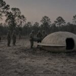 Illustration of an egg-shaped craft crash-landed in scorched sand near Camp Polk, Louisiana with small helmeted entities and Army personnel nearby, summer 1953