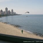 Illustration of a shrinking parachute-like object descending toward the Chicago lakefront with a green-suited figure pacing the shore, April 8, 1954