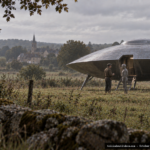 Illustration of a man in calm conversation with a humanoid figure near a landed craft in rural France, October 4, 1954