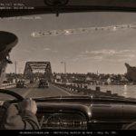 Two airmen in a car on U.S. Route 1 pointing at a long, glassy, polka-dotted tube crossing the sky near the Portsmouth toll bridge, July 1951